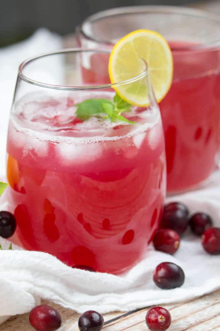 Juice in a glass with ice, mint and lemon slice with cranberries on a white flour sack