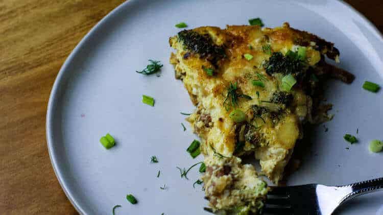 Sausage Frittata with broccoli and mushrooms on a white plate garnished with fresh herbs.