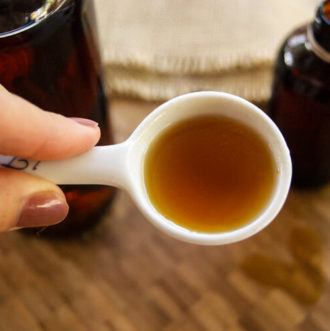 Vanilla bean extract on a spoon with a bottle next to it.