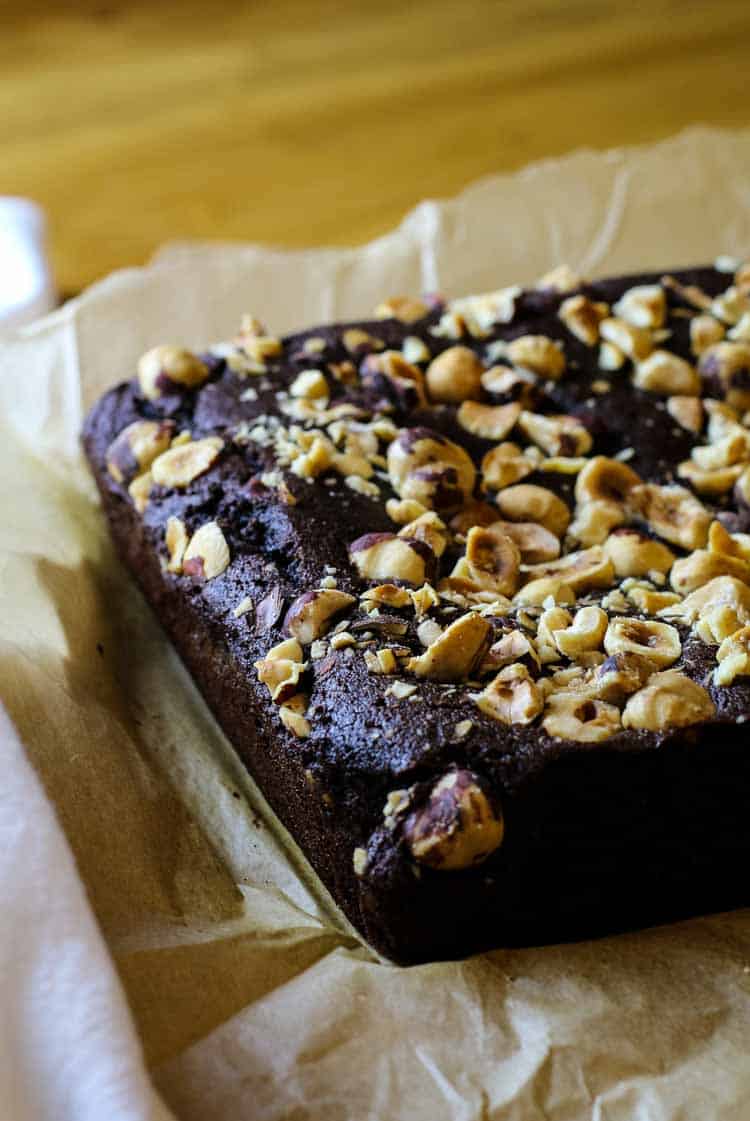 Baked coconut flour brownies with nuts on top with parchment paper.