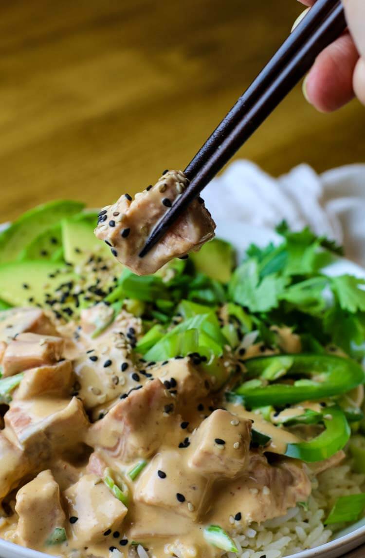 Piece of salmon in creamy sriracha mayo poke sauce with chopsticks.