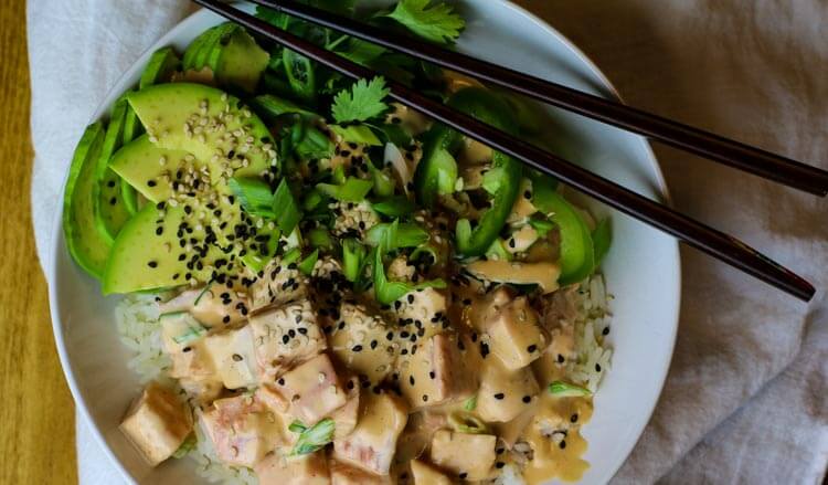 Creamy salmon poke with sliced avocado, greens and topped with sesame seeds.