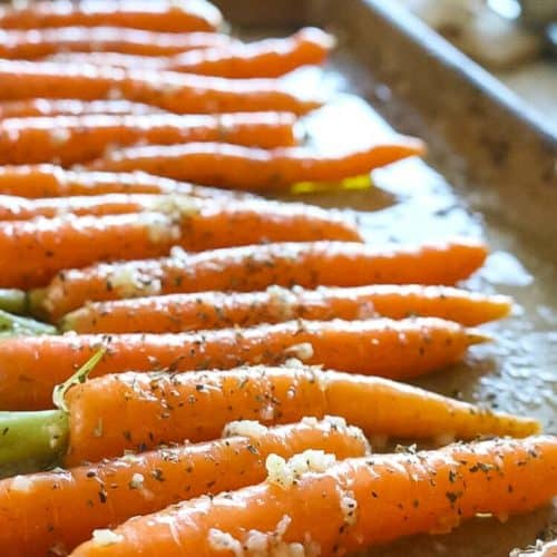 Small carrots on a baking sheet with garlic chunks.