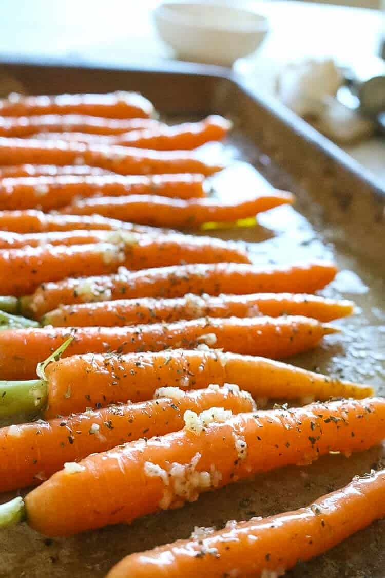 Small carrots on a baking sheet with garlic chunks. 