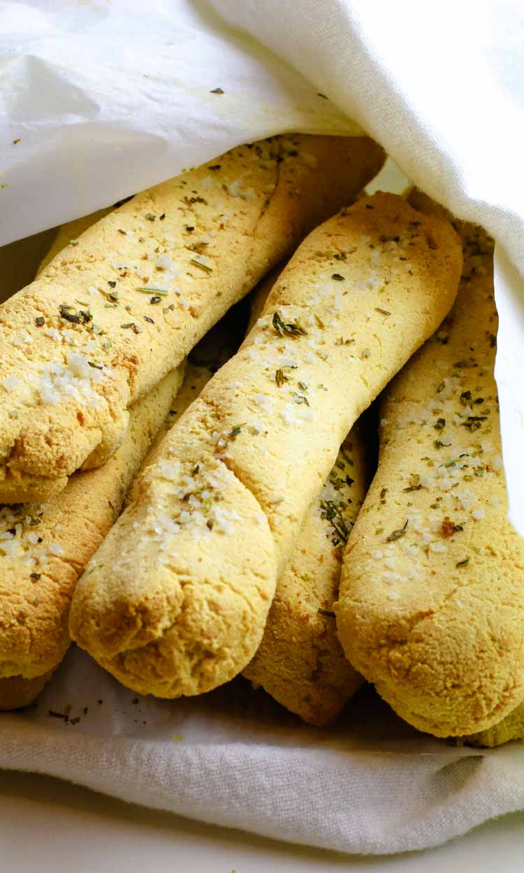 Low Carb bread sticks wrapped in a white towel. Bread sticks have seasoning on them with Italian seasoning and coarse salt.
