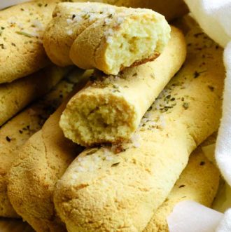 Low carb bread sticks seasoning with Italian seasoning and garlic salt. One bread stick is broken in half to expose the crumbly and chewy texture of the bread sticks.