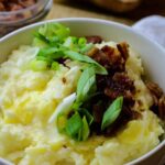 Mashed potatoes in a bowl with bacon bits and scallions.