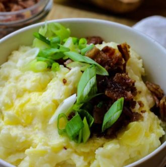 Mashed potatoes in a bowl with bacon bits and scallions.