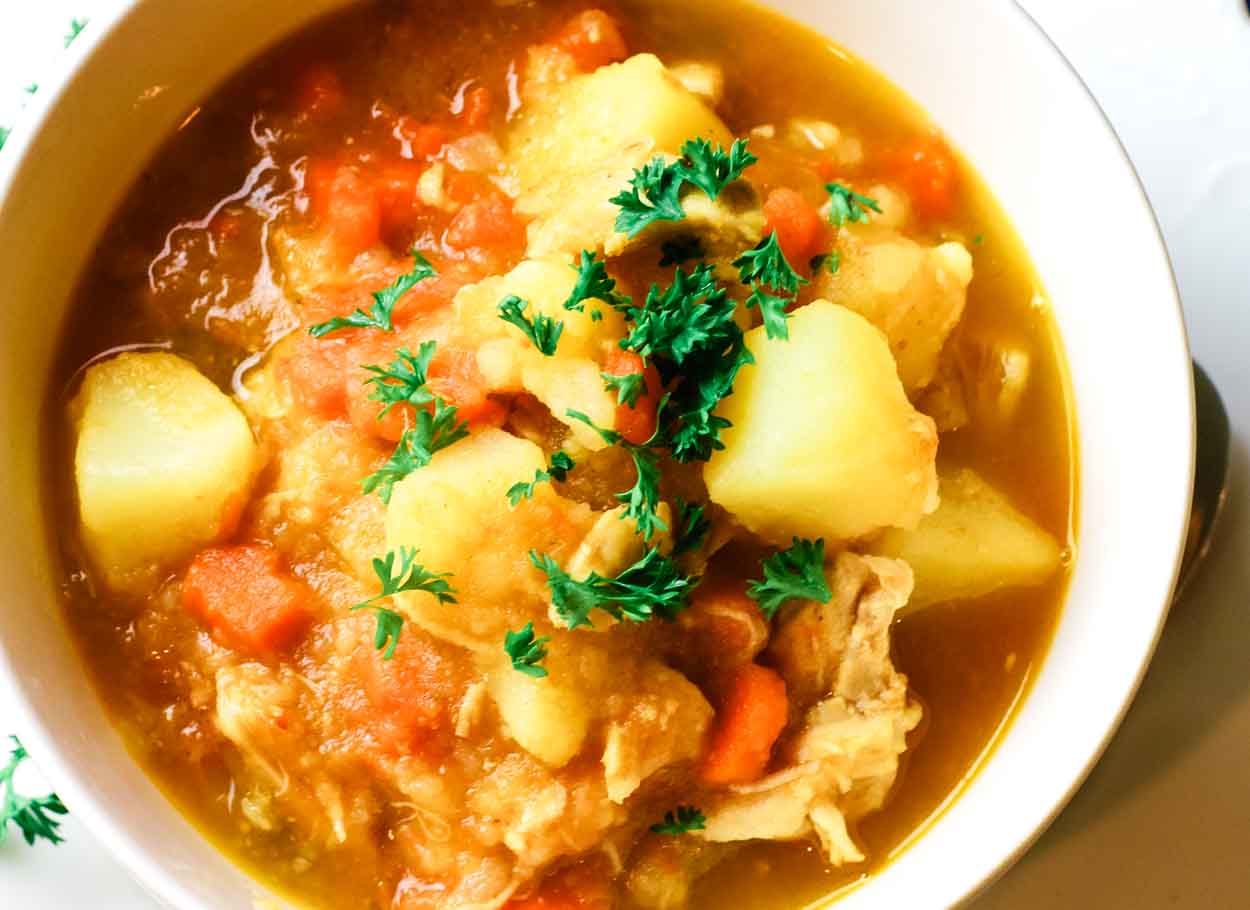 White bowl of chicken stew with potatoes and veggies.