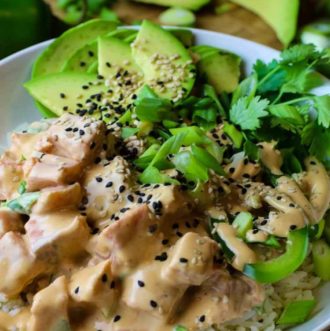 Salmon poke in a white bowl on a bed of white rice with avocado, cilantro and green onions topped.