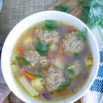 meatball soup in a white bowl with fresh dill