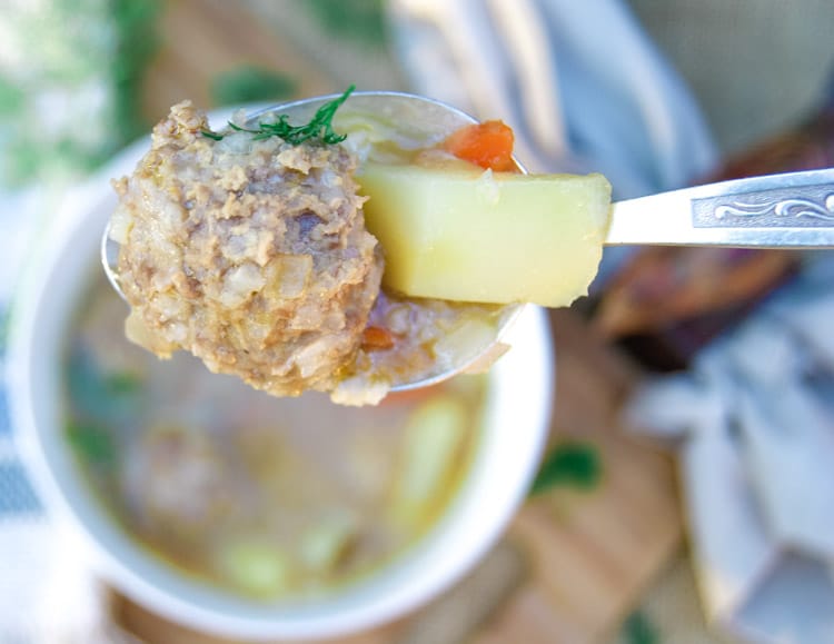 Meatball and potato chunk on a spoon over a bowl of meatball soup