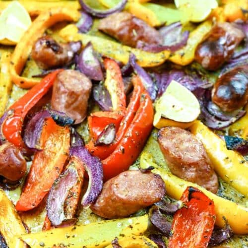 Red, orange and yellow bell peppers with sausage and red onions on a sheet pan