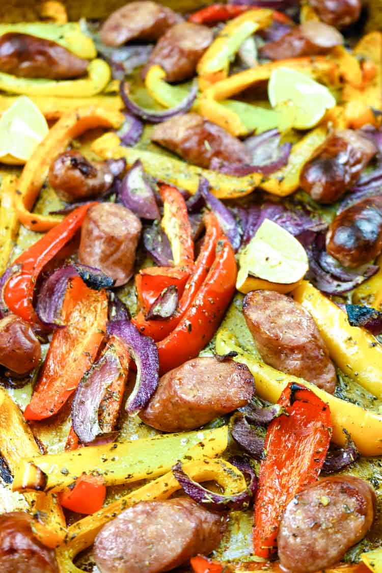 Red, orange and yellow bell peppers with sausage and red onions on a sheet pan