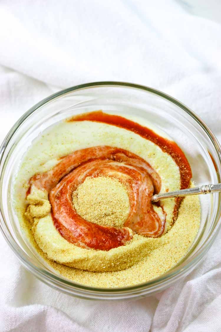 A bowl with mayonnaise, sriracha hot sauce, and garlic powder semi-combined with a spoon.