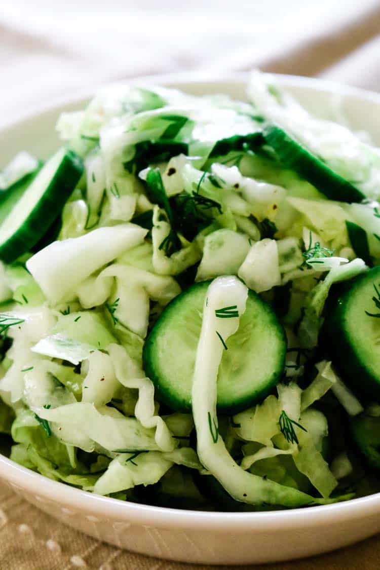 white bowl with shredded cabbage and cucumbers and dill