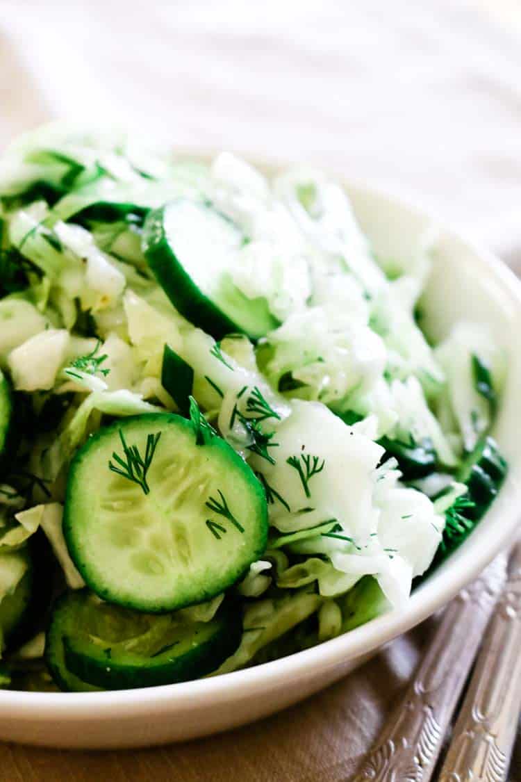 white bowl with sliced cucumbers, cabbage, and fresh dill