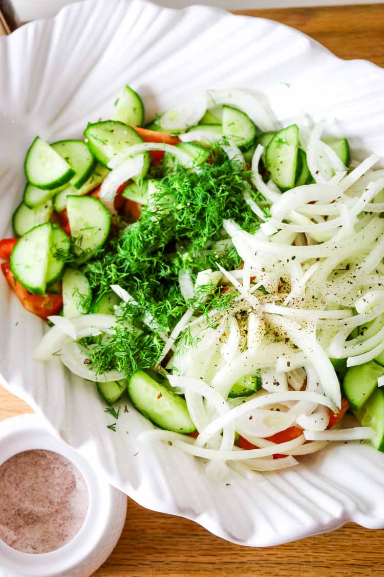 Sliced cucumbers, thinly sliced onions, and tomato wedges in a white bowl