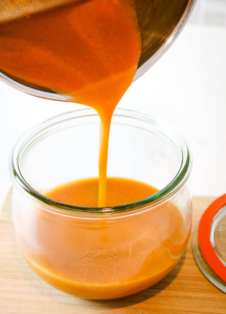 Pouring buffalo wing sauce into a smal jar for refrigeration