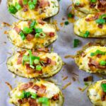Baked loaded potatoes with bacon and green onions on a baking sheet