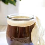 Homemade worcestershire sauce in a small weck jar with white tie and plant in the background