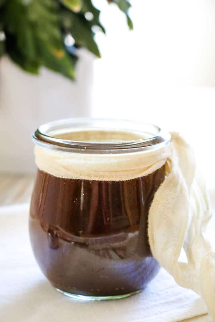 Homemade worcestershire sauce in a small weck jar with white tie and plant in the background