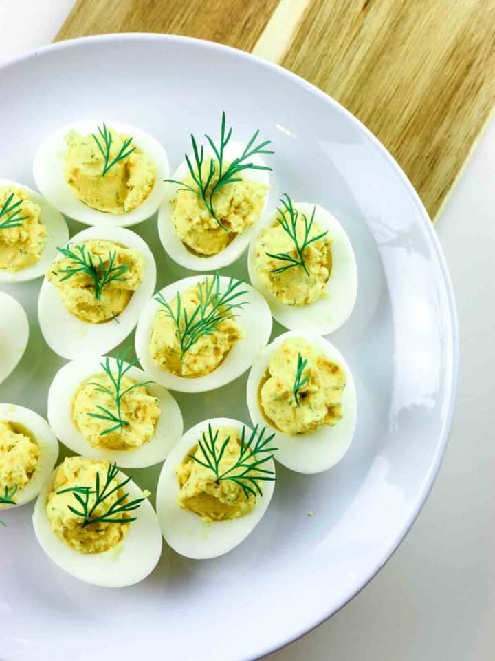 Deviled eggs on a platter and wooden cutting board.