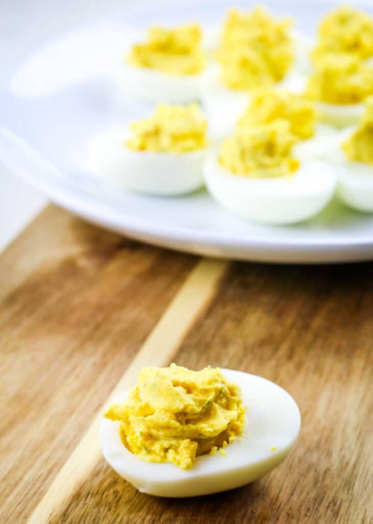 Deviled egg on a wooden cutting board with platter in the background.