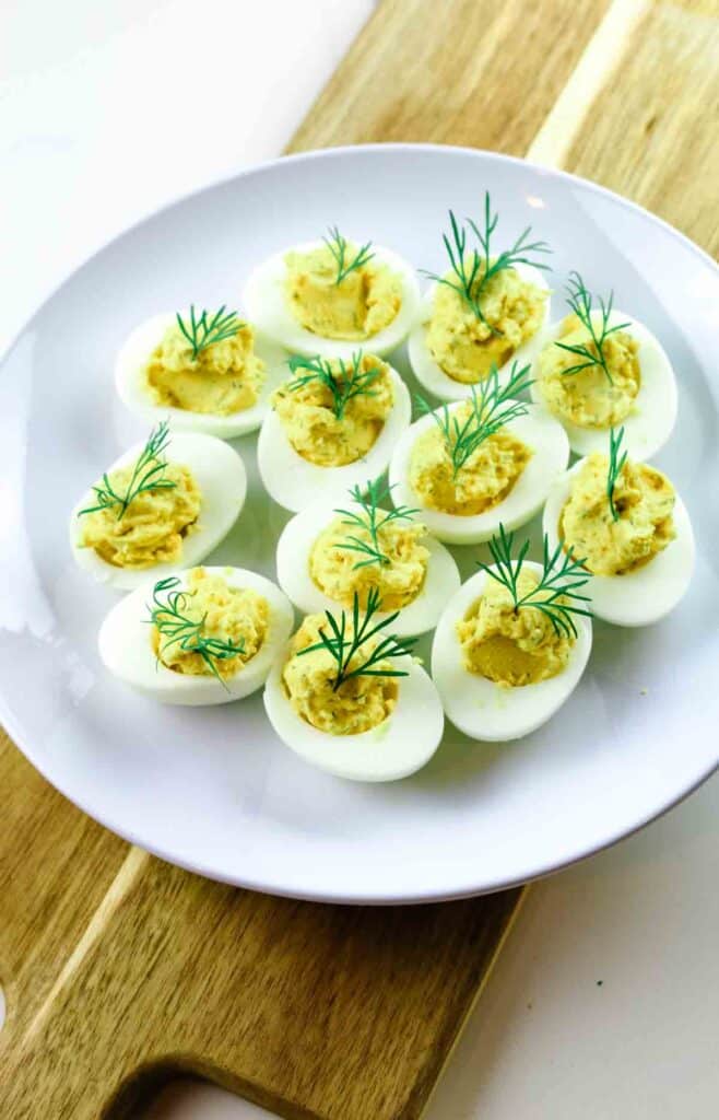 Deviled eggs on a white platter and a board with dill garnish.