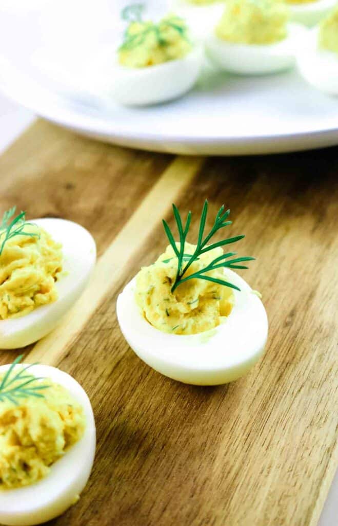 Deviled egg with a sprig of dill as garnish on a cutting board.