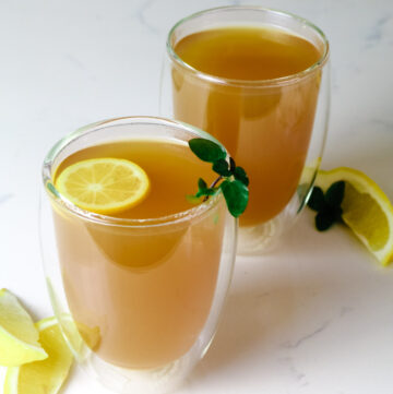 Two mugs of Honey Citrus Mint Tea with lemon slices, wedges and fresh mint.