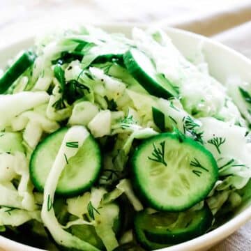 Shredded cabbage with cucumbers in a white bowl.