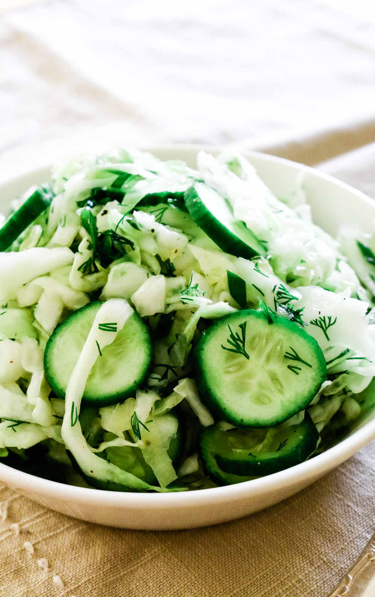 Shredded cabbage with cucumbers in a white bowl.