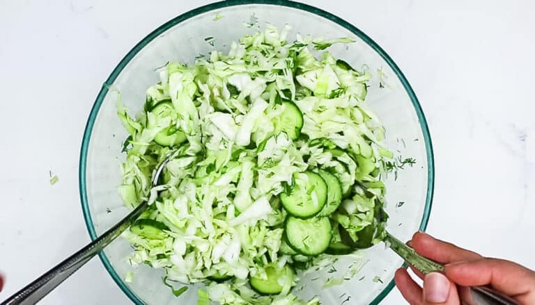 Salad being tossed in a bowl with cabbage and cucumbers