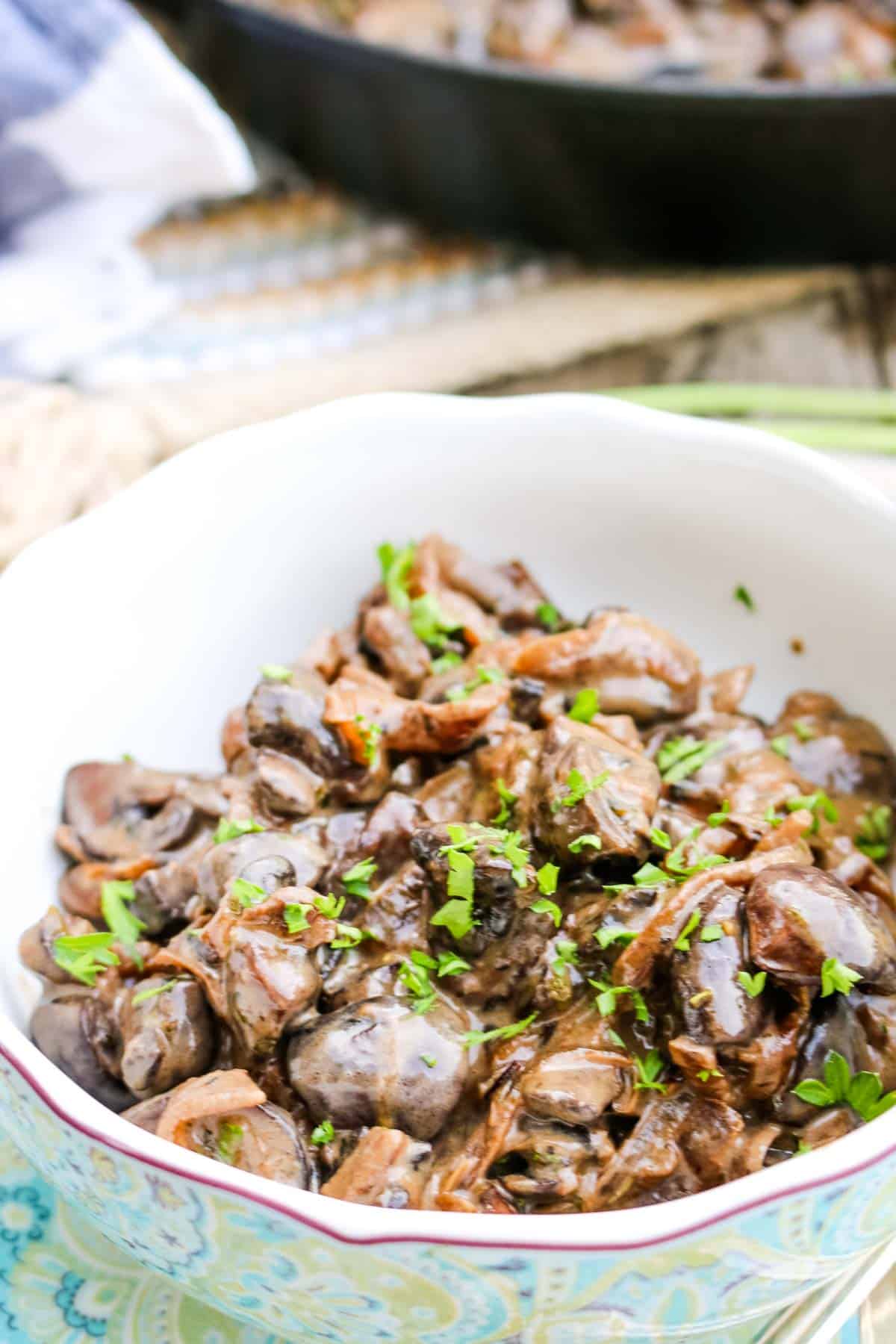 Creamed Mushrooms in a bowl with cast iron skillet in the back and parsley garnished