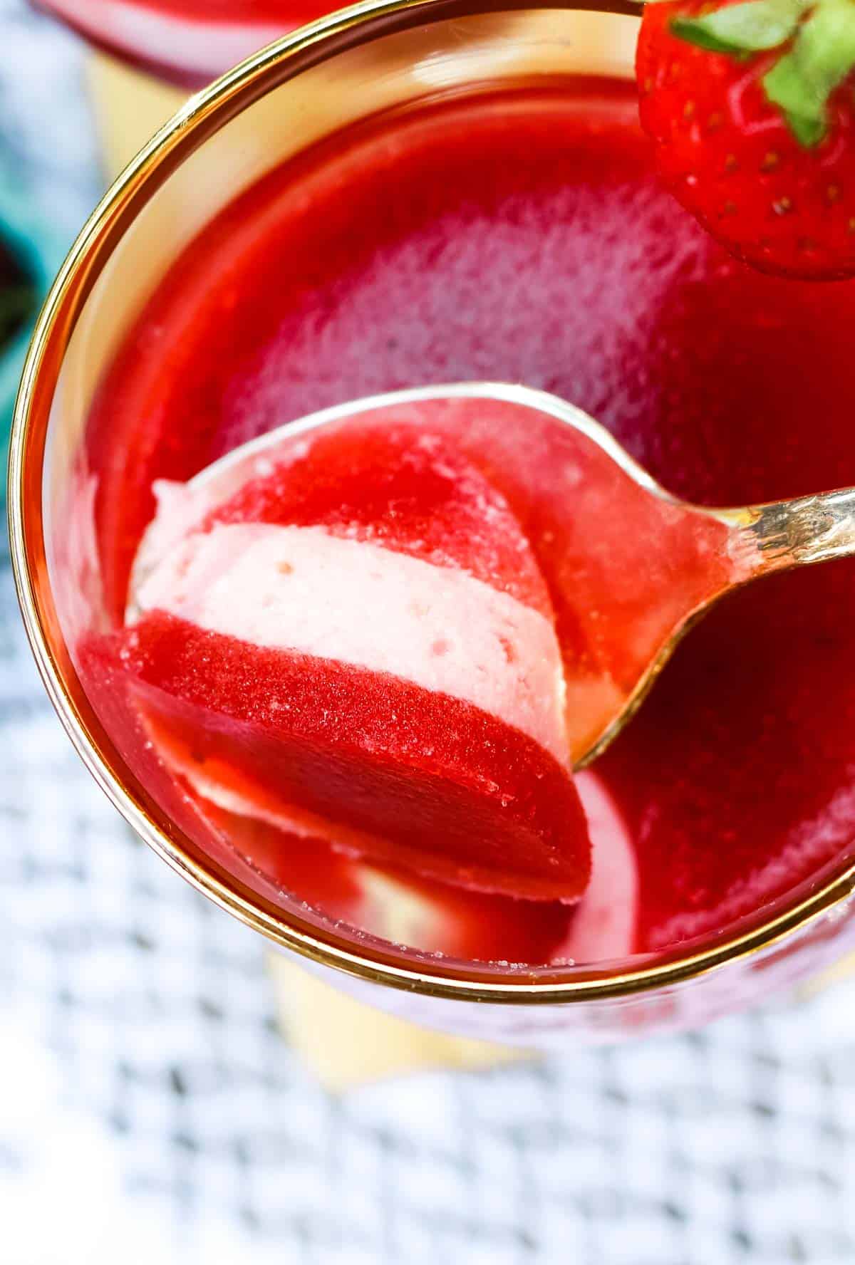 Strawberry gelatin dessert layered with cream gelatin and a spoon diggin in.