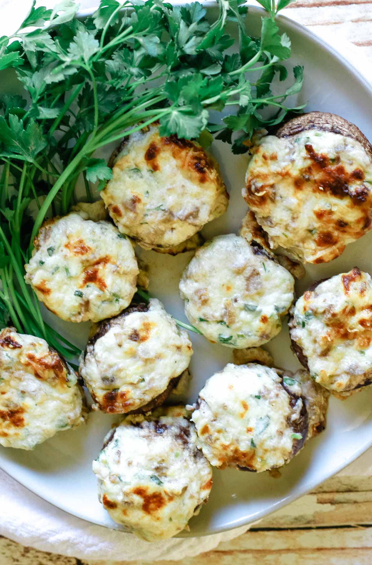A white plate of cheesy stuffed mushrooms with parsley garnish