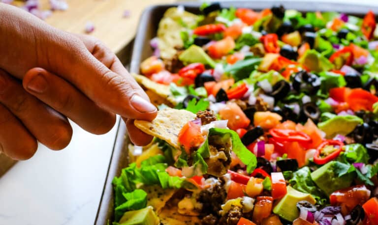 hand pulling a chip from ultimate sheet pan nachos