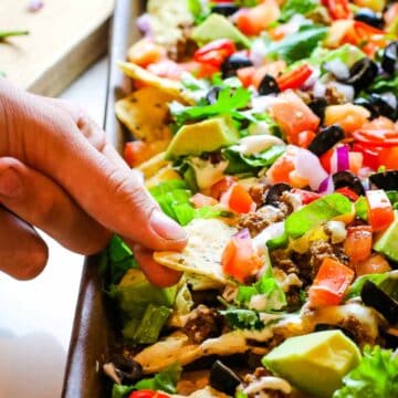 hand pulling one chip from sheet pan nachos