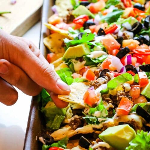 hand pulling one chip from sheet pan nachos