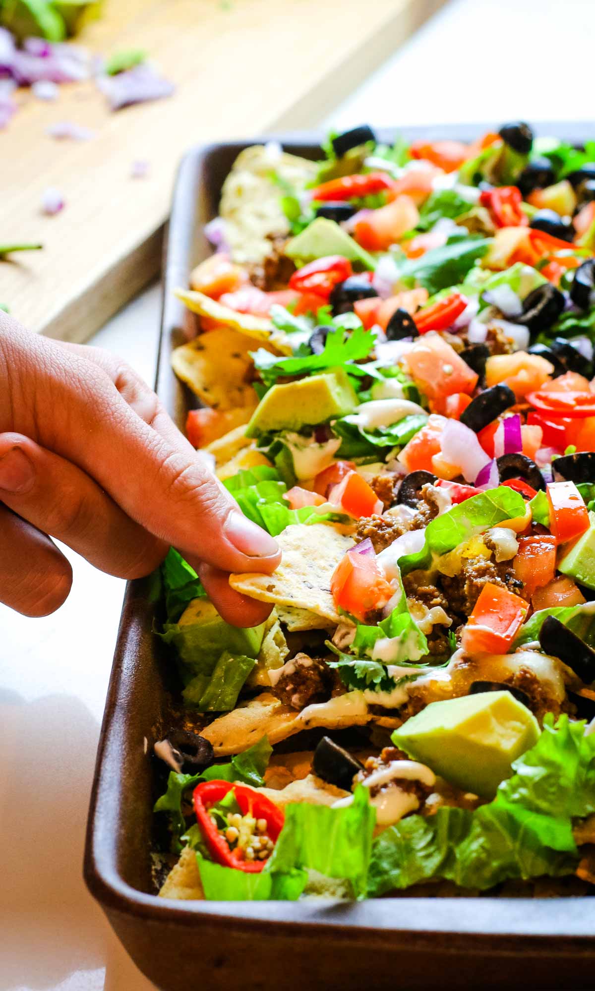 hand pulling one chip from sheet pan nachos