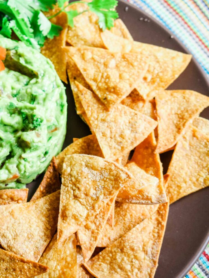 homemade tortilla chips on a brown plate with guacamole on the side