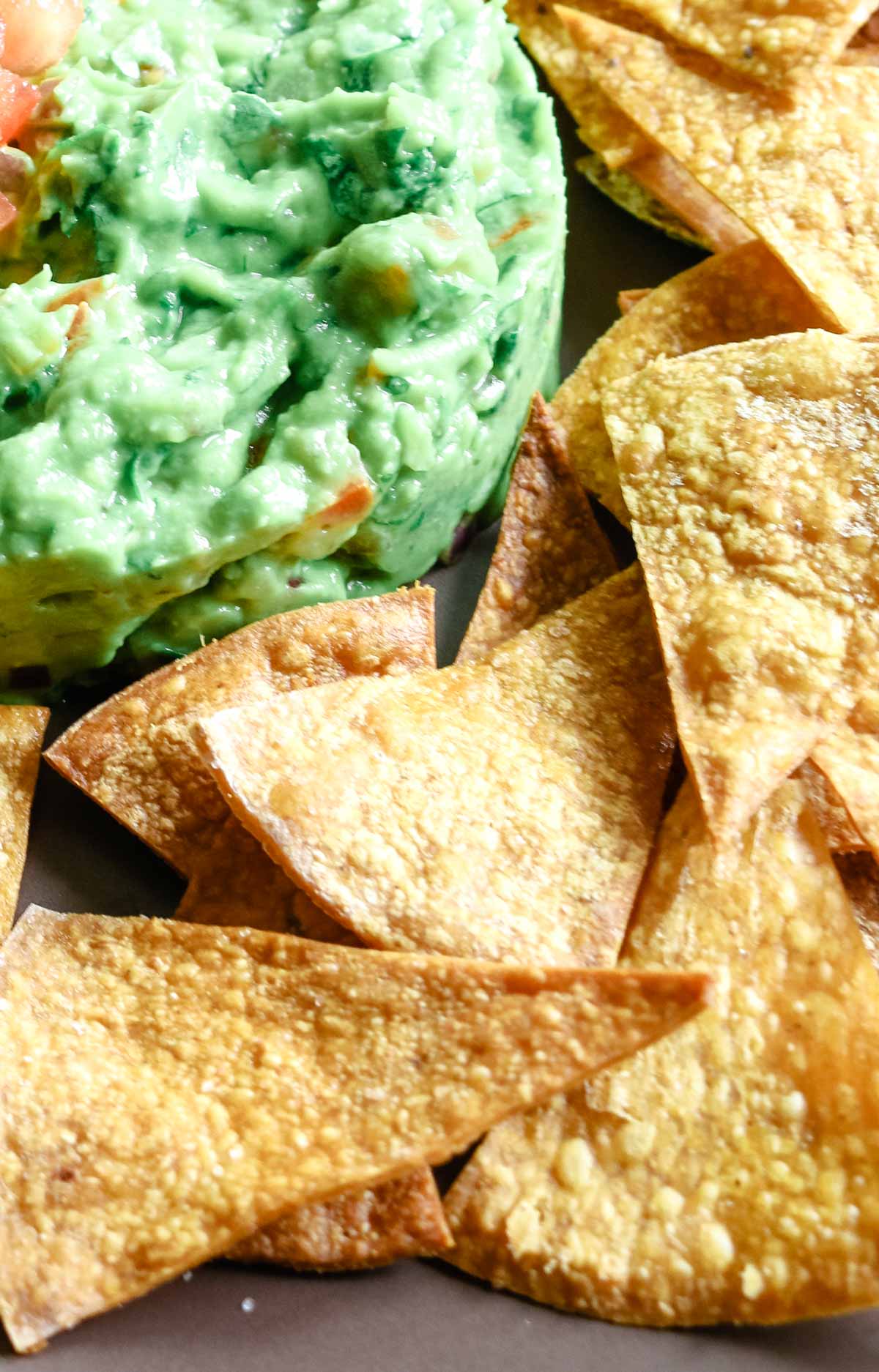 homemade tortilla chip triangles on a brown plate with guacamole