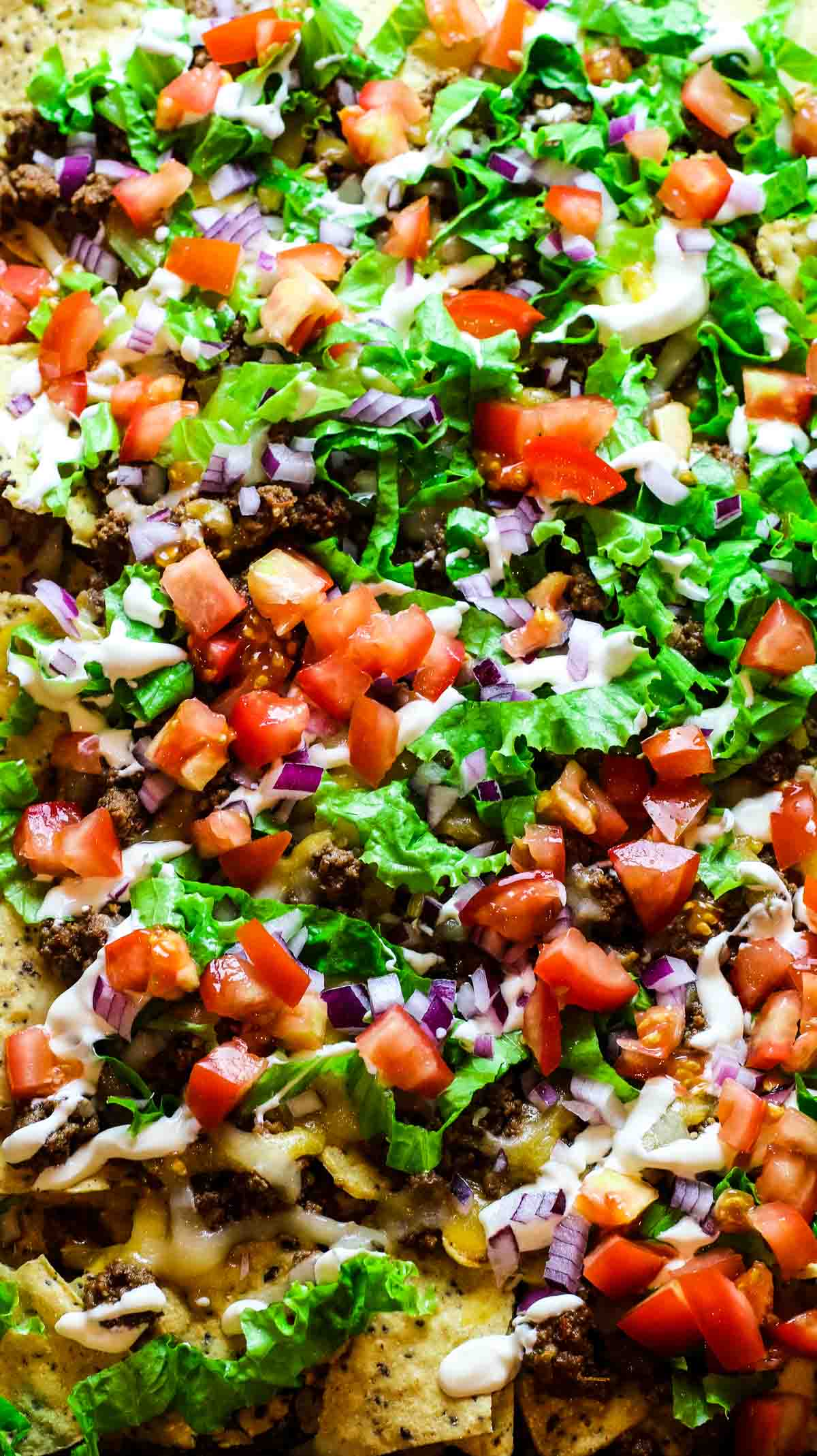 sheet pan nachos with toppings tomatoes and red onions and lettuce