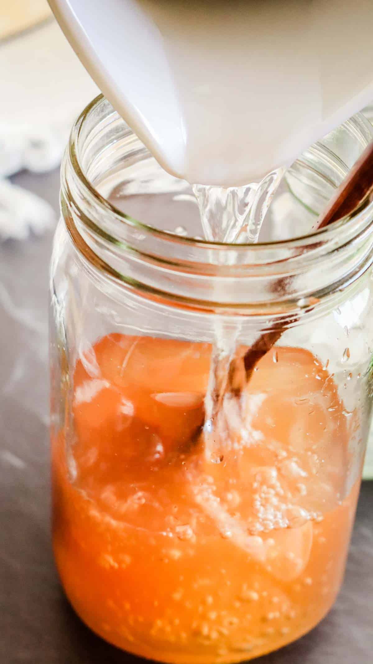dissolving tomato paste in a large mason jar with water and wooden spoon