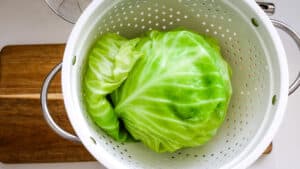 Cooked green cabbage in a colander on wooden board