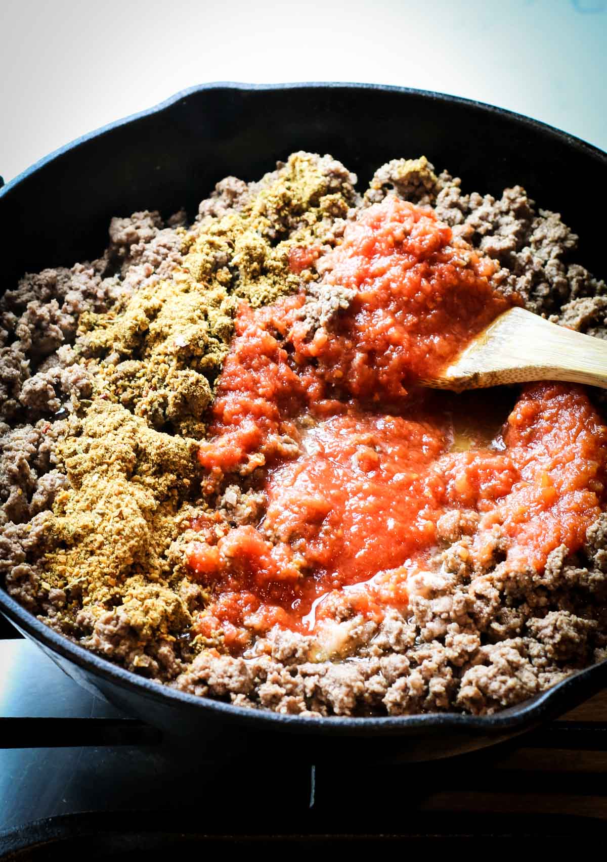 Ground beef in cast iron skillet with taco seasoning and tomato sauce over it