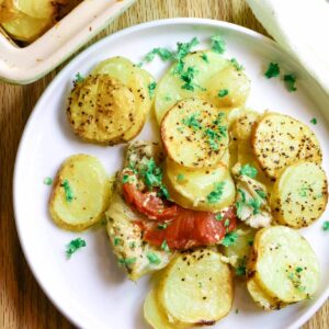 scalloped potatoes on a white dish with tomatoes and chicken.