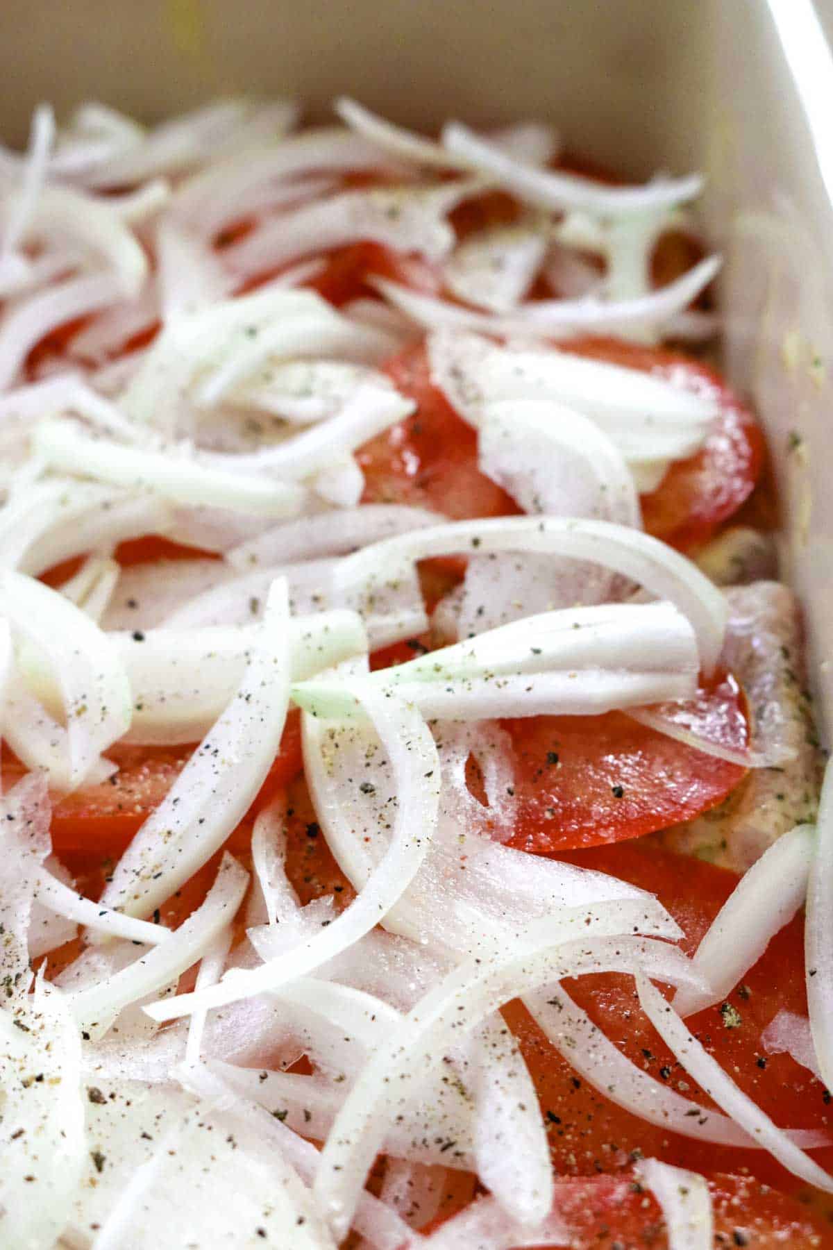 sliced tomatoes and onions in a casserole dish