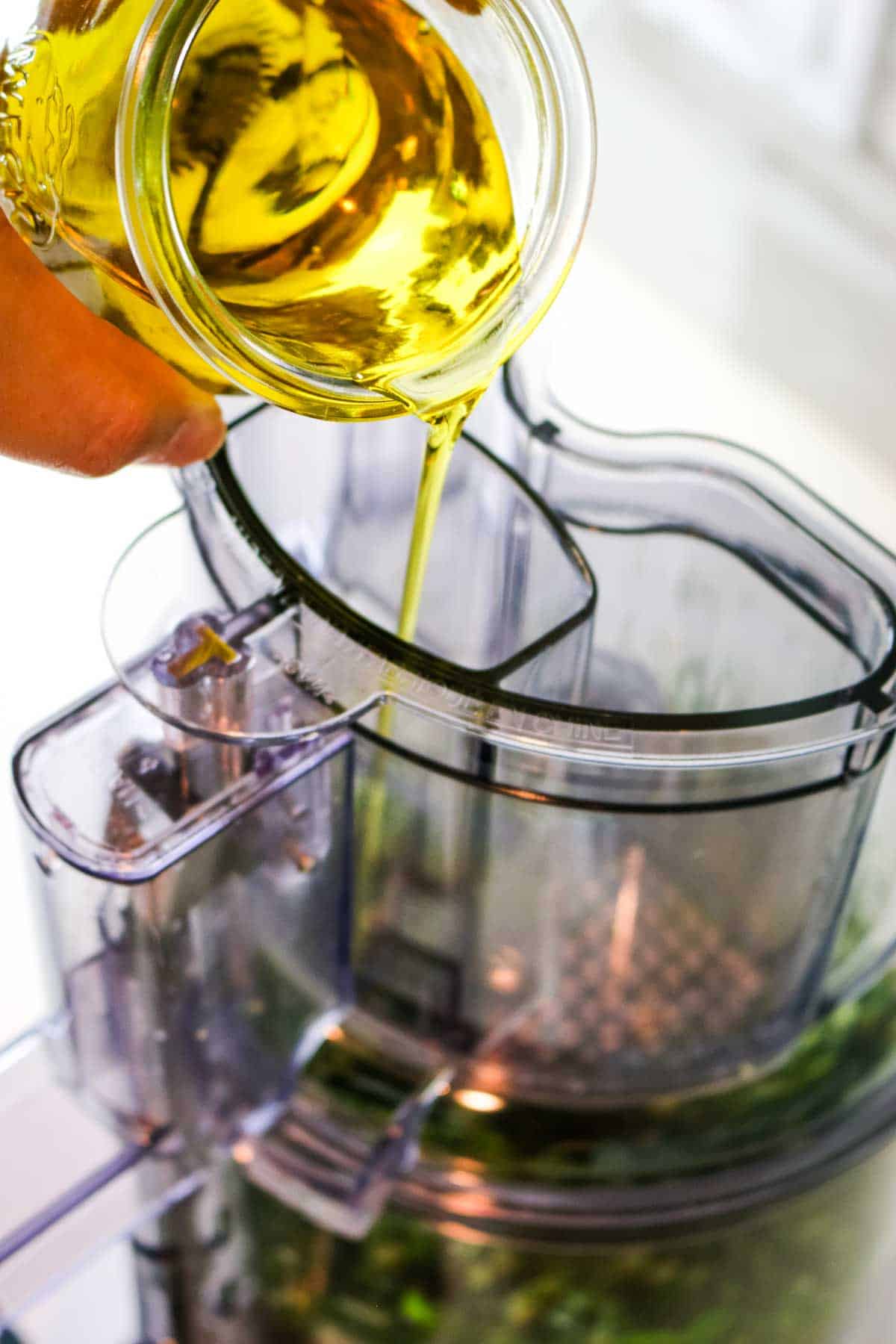 olive oil being poured in stream into food processor chute